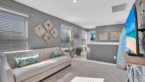 Ein modernes Wohnzimmer mit einem beigefarbenen Sofa, Wanddekoration und einem großen Fernseher.