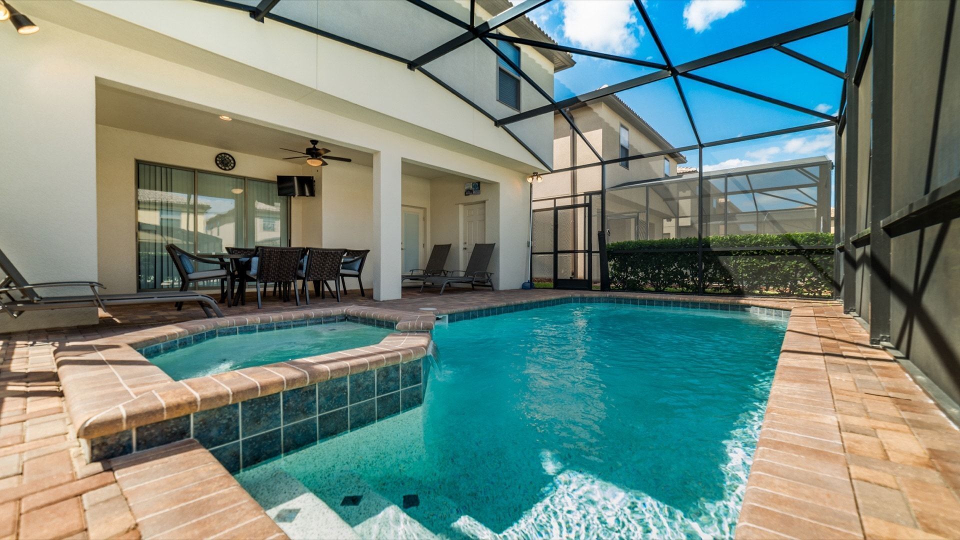 Una piscina con dos áreas separadas, un porche cubierto con mobiliario exterior y una vista despejada del cielo a través de una estructura de cristal.