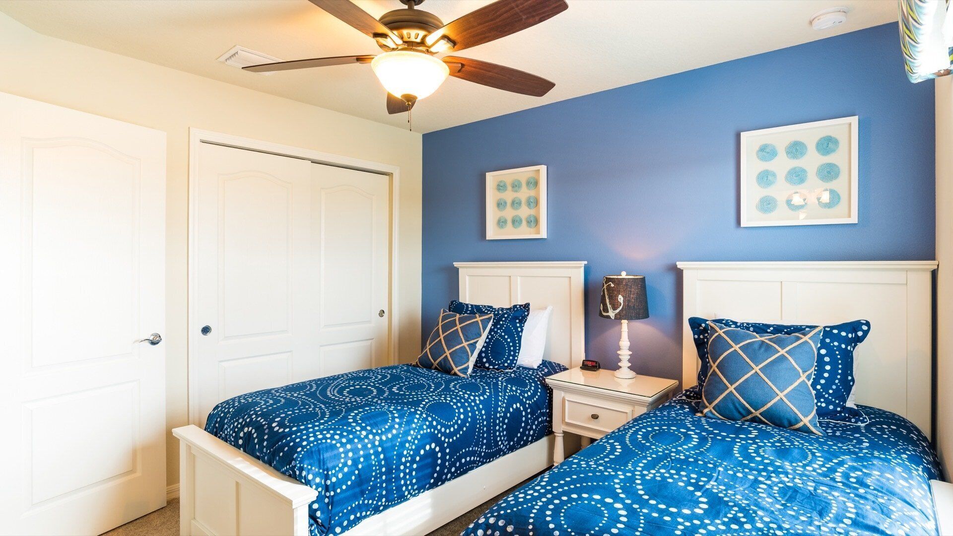 A bedroom with two beds, a ceiling fan, and artwork on the wall.