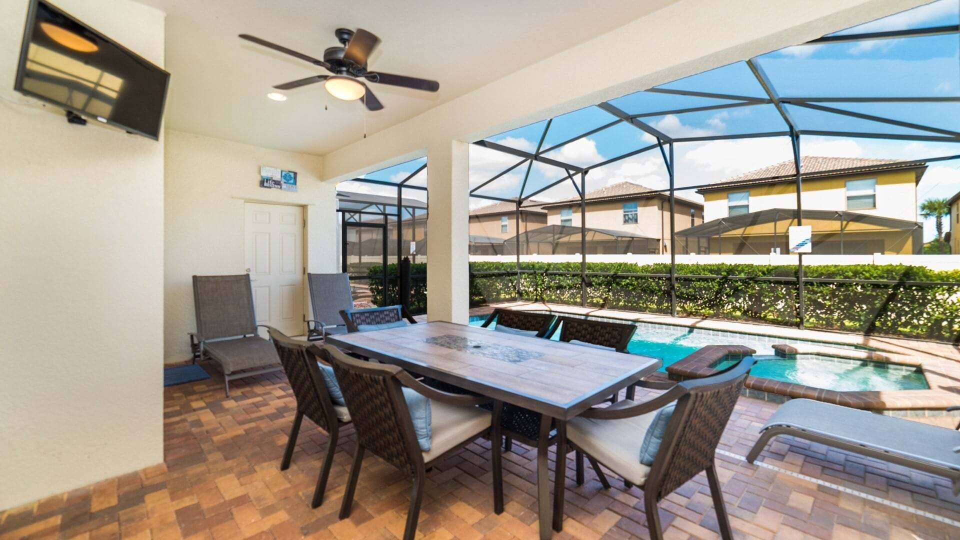 An outdoor patio with a pool, dining table, chairs, and a ceiling fan.