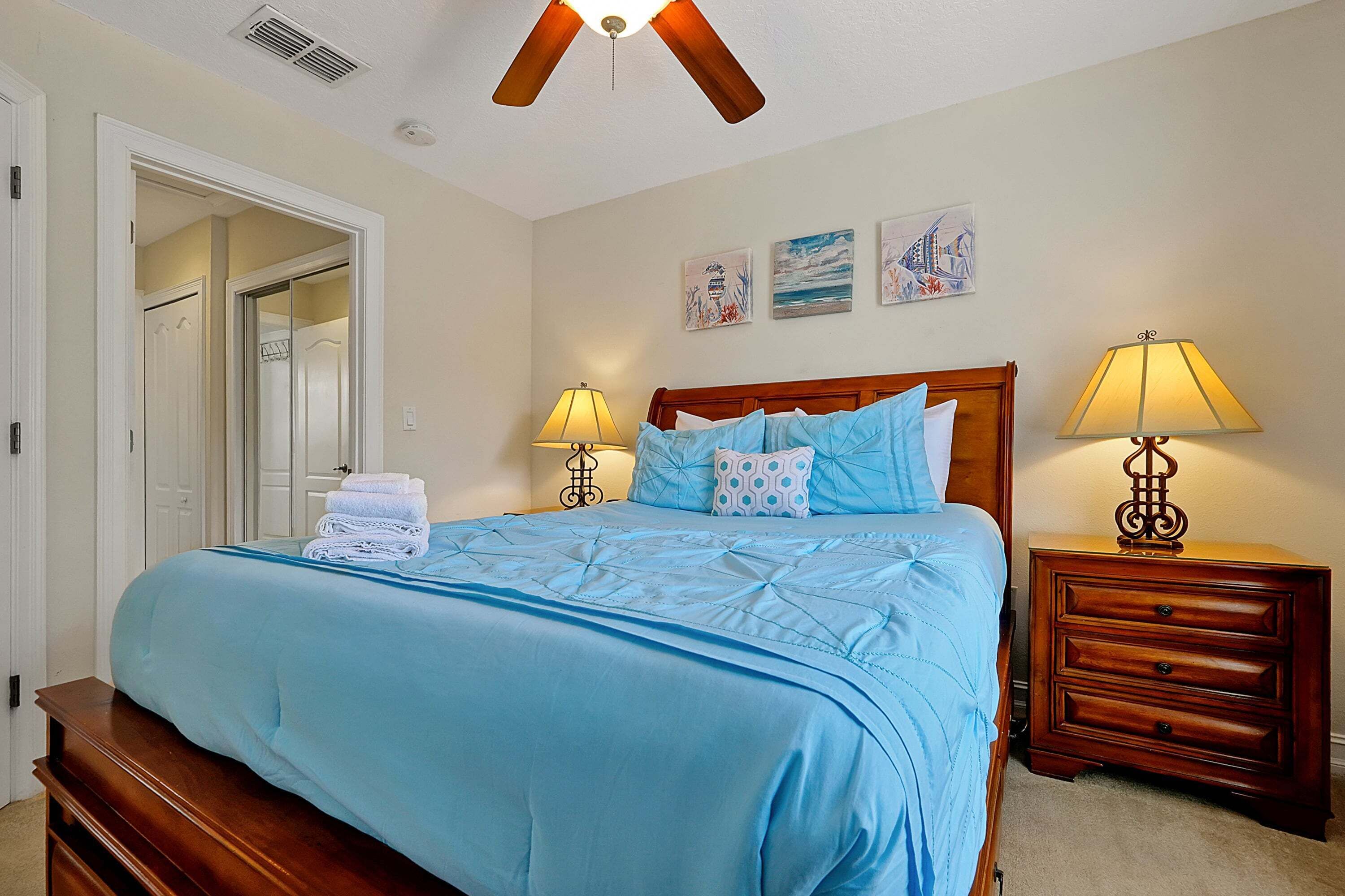 A bedroom with a bed, two bedside tables with lamps, a wooden headboard, and a closet with a door.