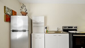A compact kitchen with a refrigerator, a sink, a stove, and white cabinetry. - 7407 Excitement Drive, Kissimmee, Unit A, 1 BED (Kissimmee)