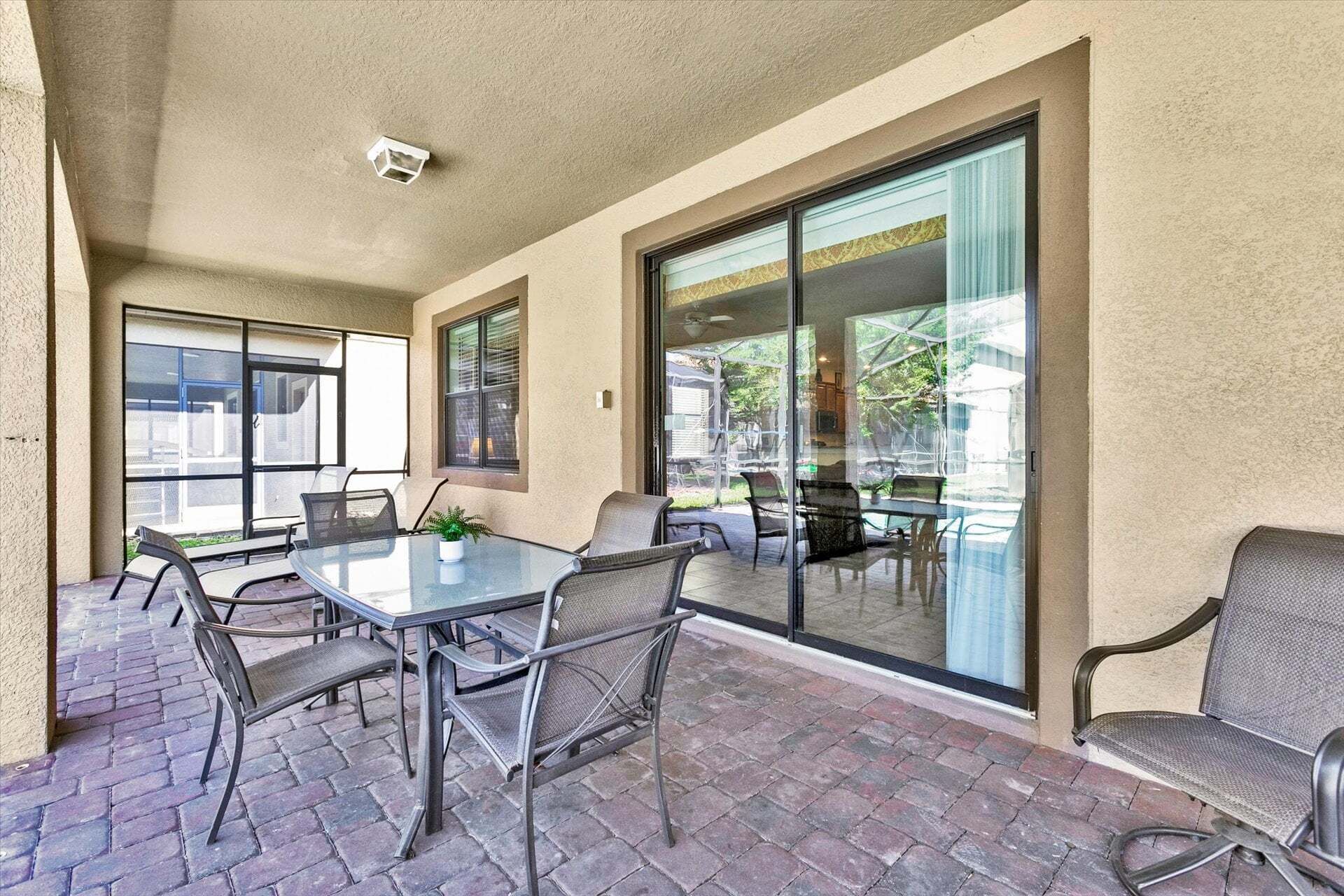 An outdoor patio with a glass table and chairs, a potted plant, and a view of the backyard.