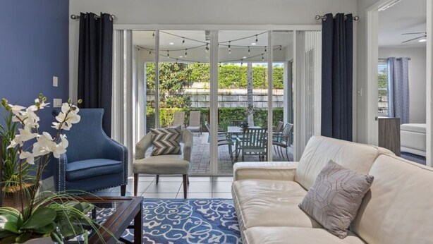 A modern living room with a sofa, armchair, and coffee table. There is a large sliding glass door leading to an outdoor patio with chairs and a table. - 360-7-pc-large and Luxury Villa (Kissimmee)
