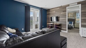 A modern living room with a black leather sofa, a flat-screen TV, and a wooden accent wall. - 360-7-pc-large and Luxury Villa (Kissimmee)