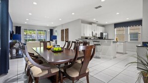 A modern kitchen with white cabinets, a central island, and a dining area with a wooden table and chairs. - 360-7-pc-large and Luxury Villa (Kissimmee)