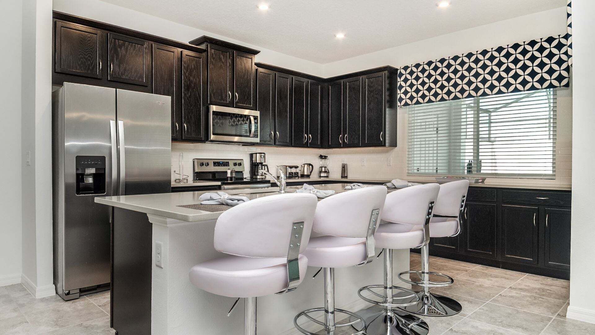 A modern kitchen with dark cabinets, stainless steel appliances, a central island with bar stools, and a patterned window valance.