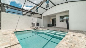 A swimming pool with a clear blue water, surrounded by a patio area with lounge chairs and a table. - Cbp2166 (Kissimmee)