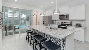 A modern kitchen with a large island, stainless steel appliances, and a view of a pool. - Windsor Island Resort 5 Bedroom East Facing Pool - P820923 (Davenport)