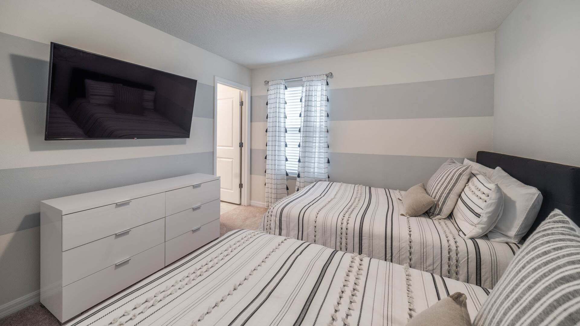 A bedroom with two beds, a TV, a dresser, and a window with curtains.