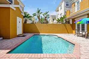Una piscina con borde de ladrillo, rodeada por un muro amarillo y una puerta blanca.