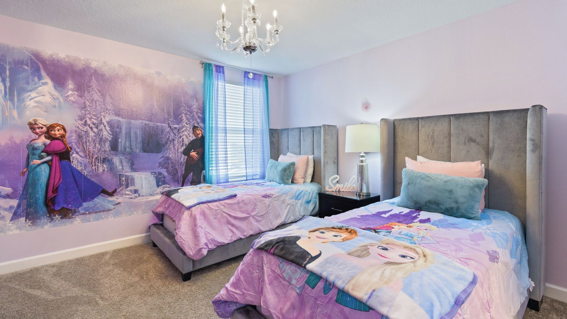 Quarto com duas camas, um mural com personagens de Frozen, um candelabro e uma janela com cortinas azuis.