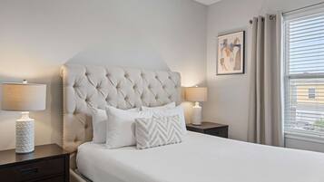 A neatly arranged bedroom with a tufted headboard, white bedding, and two bedside lamps.
