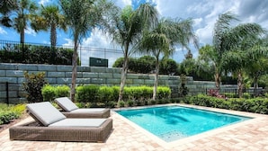 A rectangular swimming pool with a tiled deck, surrounded by palm trees and a stone wall. - 350-360 Huge Villas - Near Disney - 15 BDs (Kissimmee)
