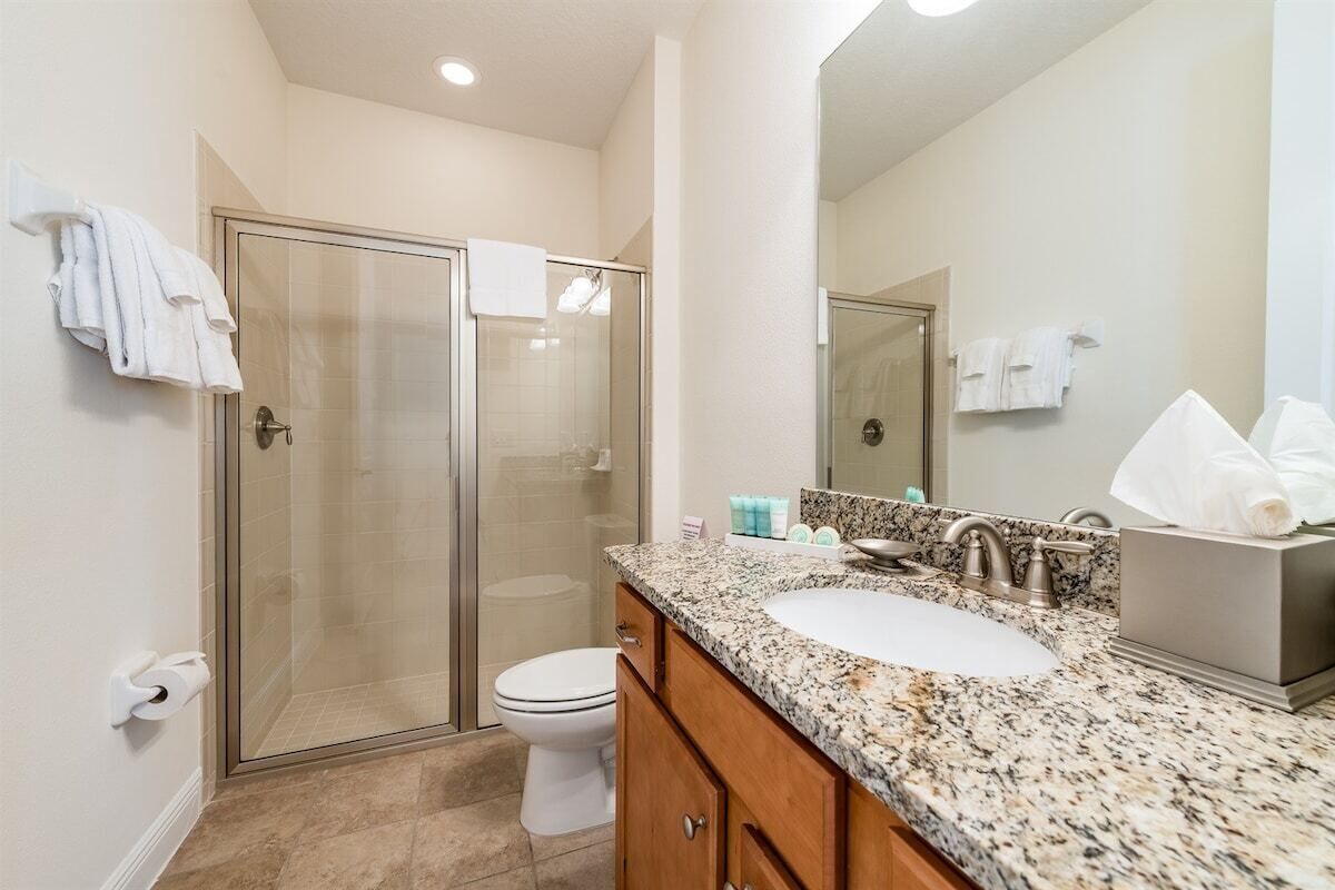 A modern bathroom with a glass shower enclosure, a white toilet, a granite countertop sink, and wooden cabinets.