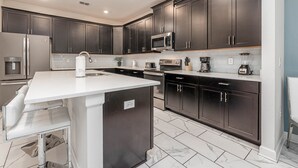 Una cocina moderna con armarios oscuros, electrodomésticos de acero inoxidable y encimera blanca.