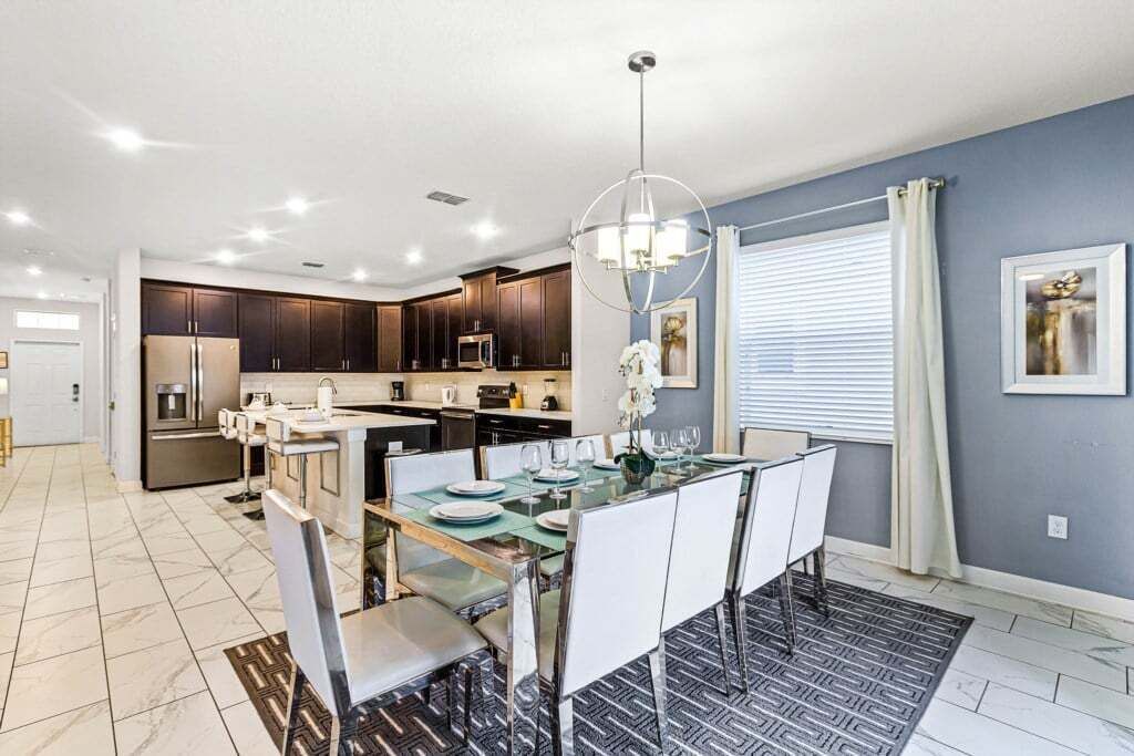 A modern kitchen with dark cabinets, a central island, and a dining area with a glass table and chairs.