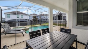 Un espacio al aire libre techado con piscina, sillas de descanso y una mesa.