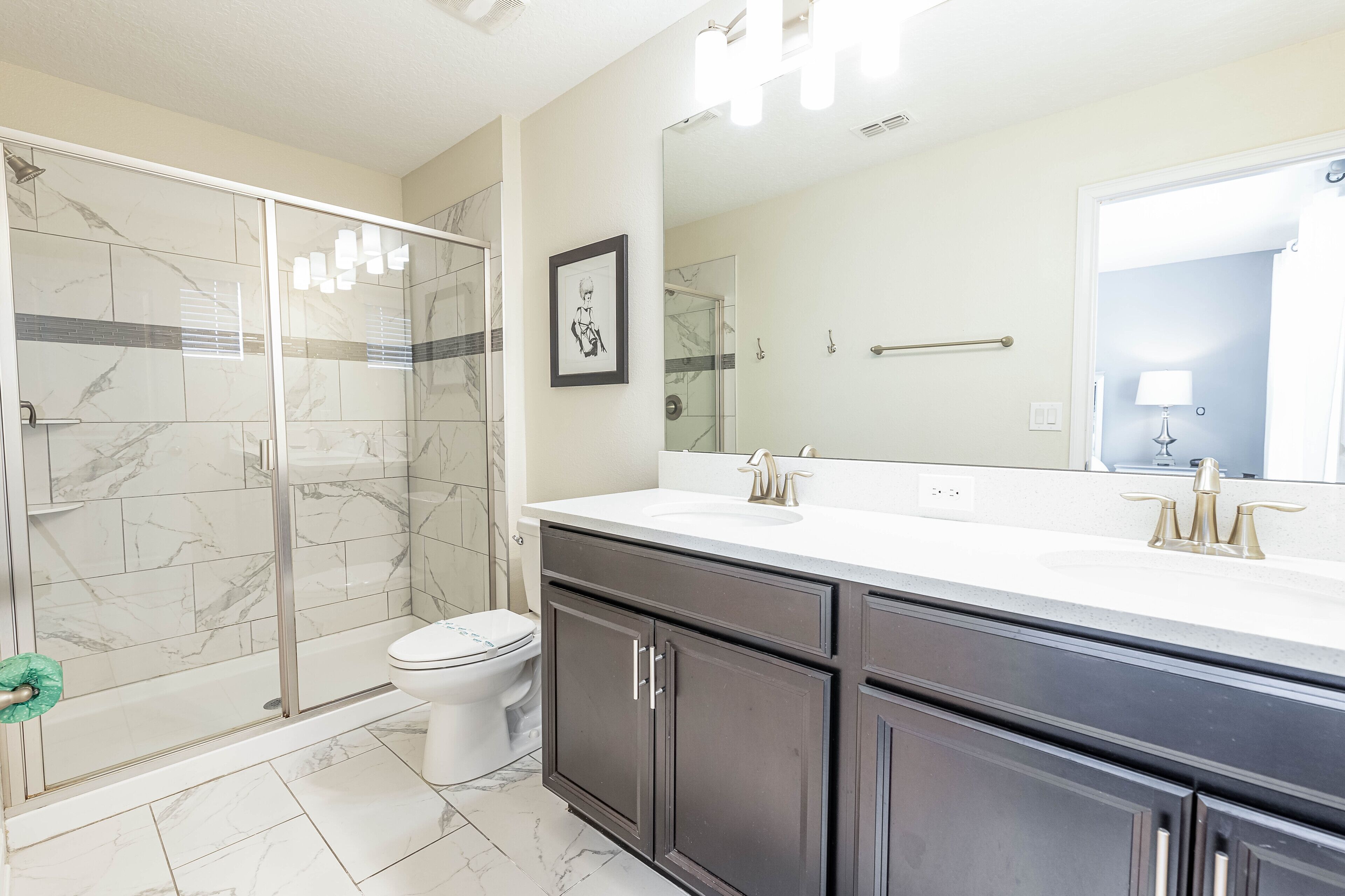 A modern bathroom with a glass shower enclosure, a toilet, and a vanity with a large mirror.