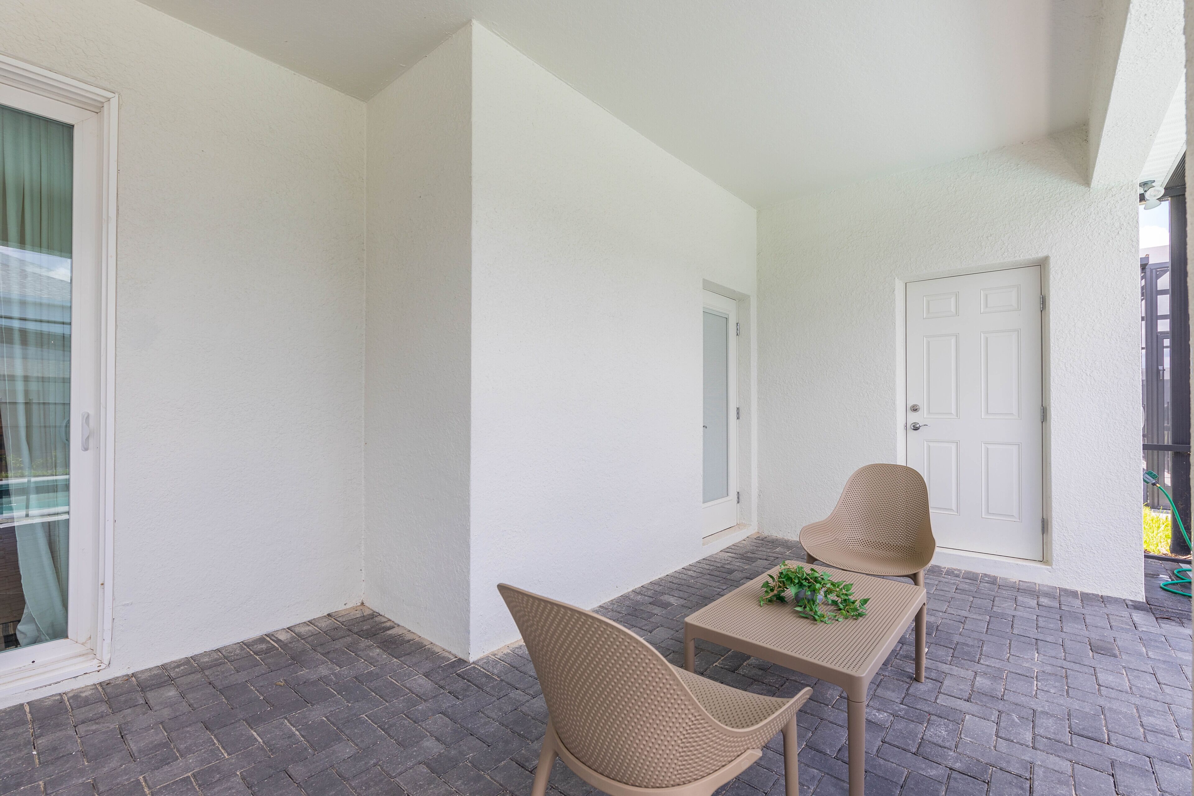 Une terrasse avec deux fauteuils en osier et une table, une porte blanche et une fenêtre avec des rideaux.