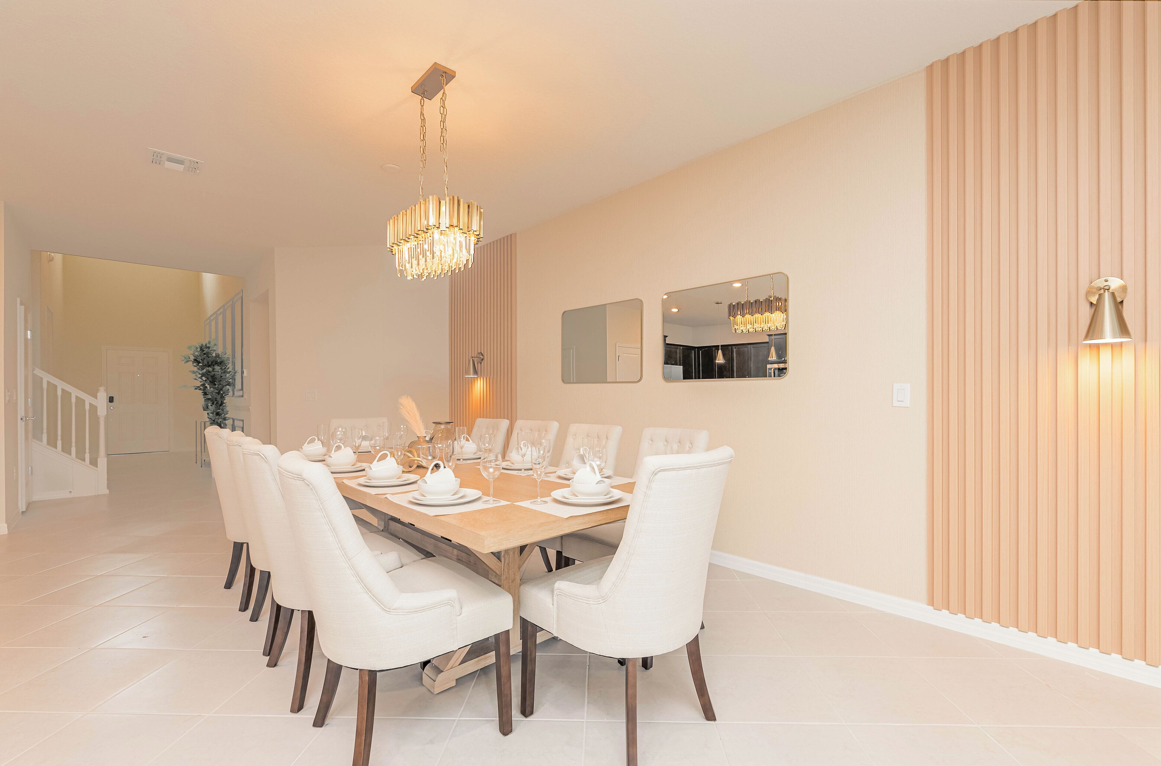 A dining area with a large wooden table set for six, surrounded by white upholstered chairs.