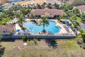 Vista aérea de un resort con una amplia piscina rodeada de palmeras y sillas de descanso.