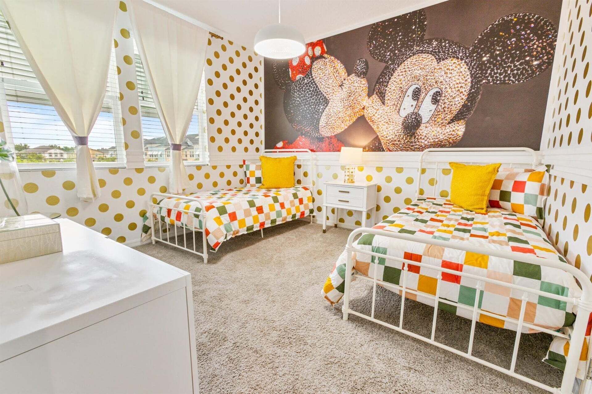 A bedroom with two beds, a white dresser, and a mural of Mickey Mouse.