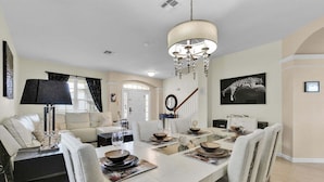 A dining area with a chandelier, a sofa, a coffee table, and a dining table set for six. - Windsor Hills Resort 6 Bedroom Private Pool Spa Home 0743 (Kissimmee)