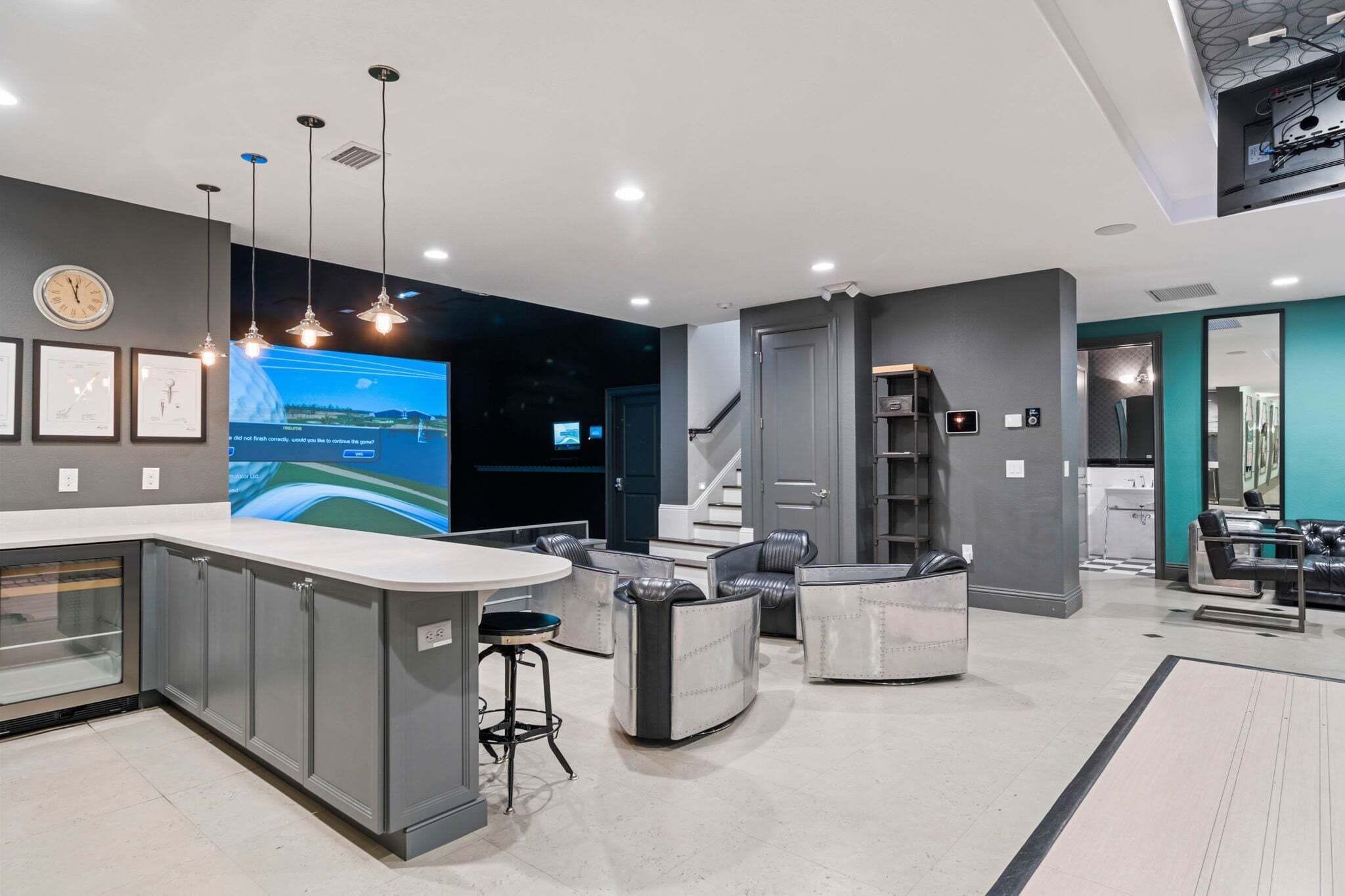 A modern kitchen with a central island, bar stools, and a large screen displaying a landscape.