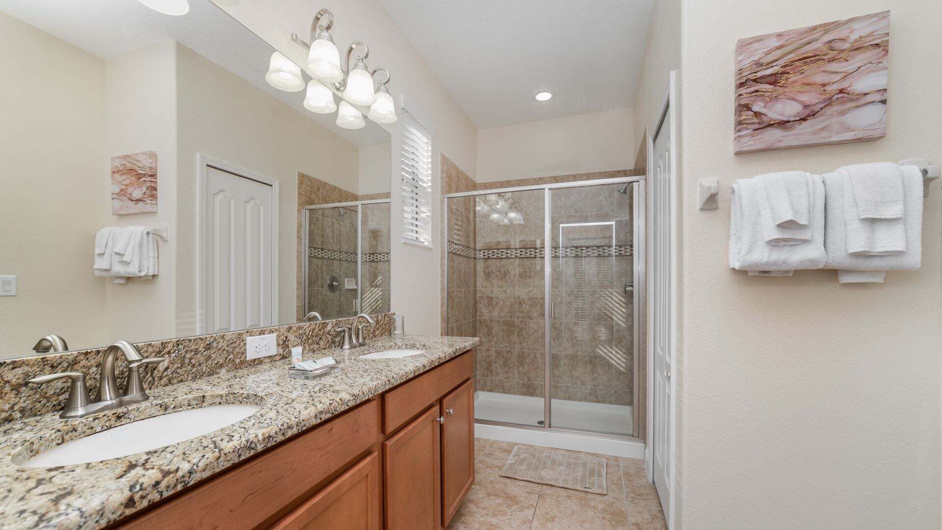 A bathroom with a double sink, a shower, and a large mirror.