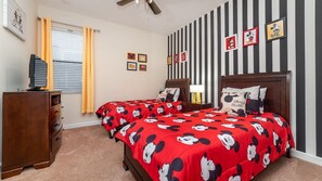 Een slaapkamer met twee bedden, een dressoir, een televisie en beddengoed met een Mickey Mouse thema.