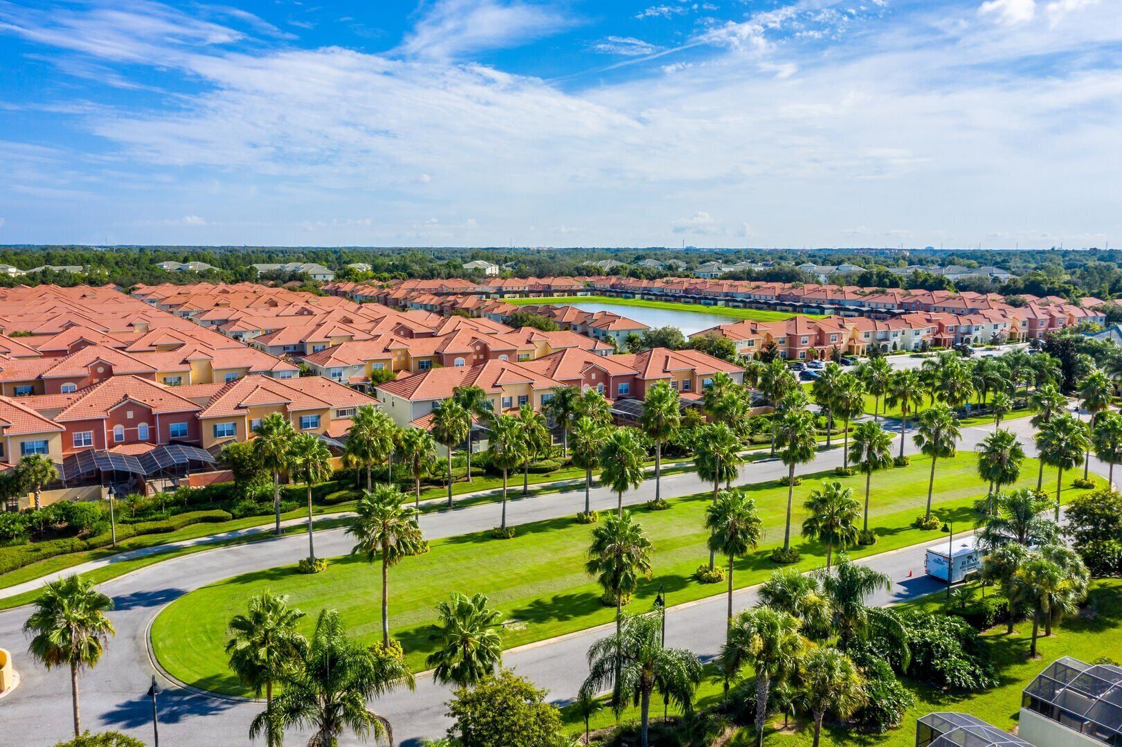 A residential area with red-roofed houses, palm trees, and a clear sky.