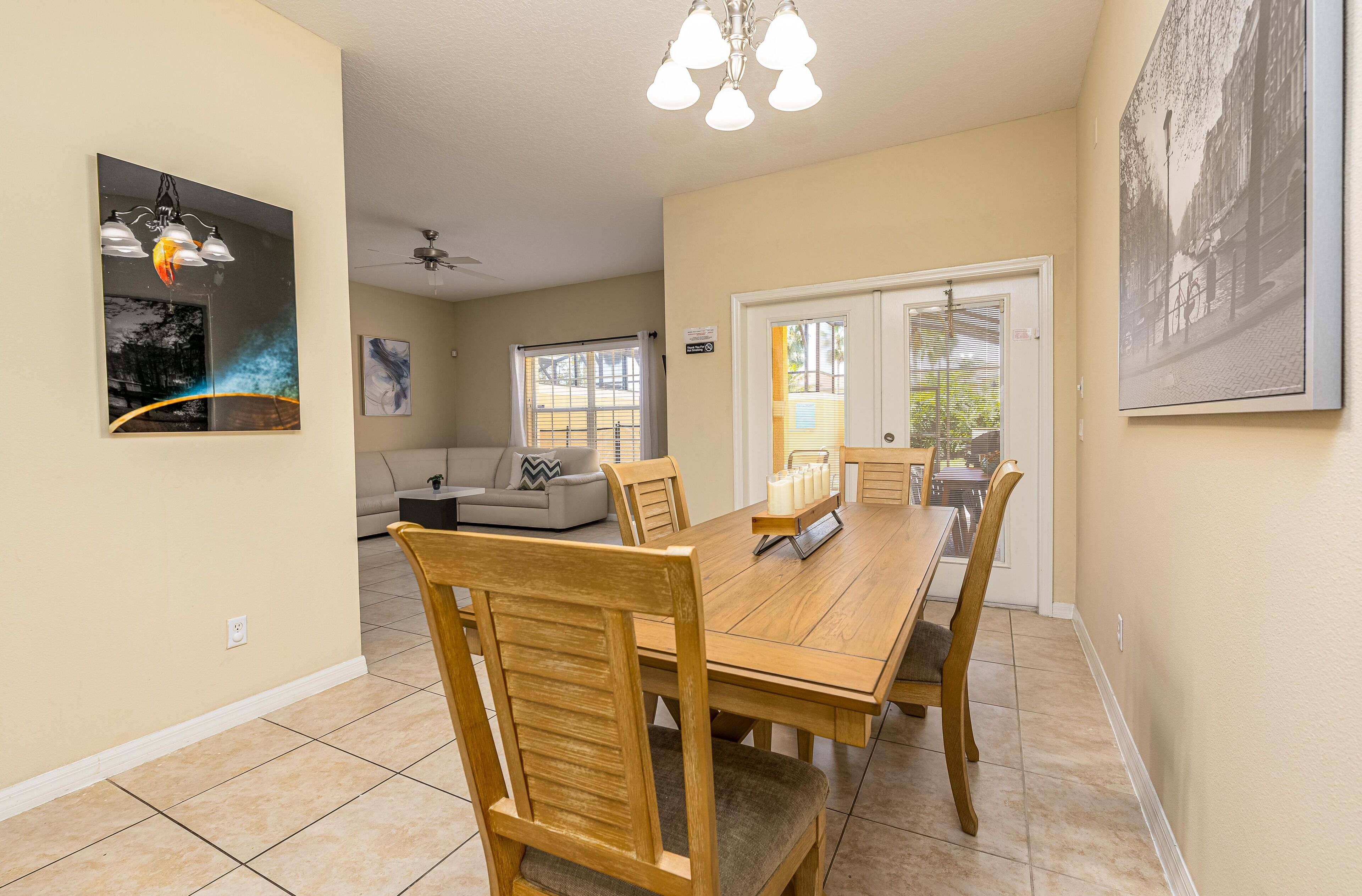 A dining area with a wooden table and chairs, a ceiling fan, and a large window with blinds.