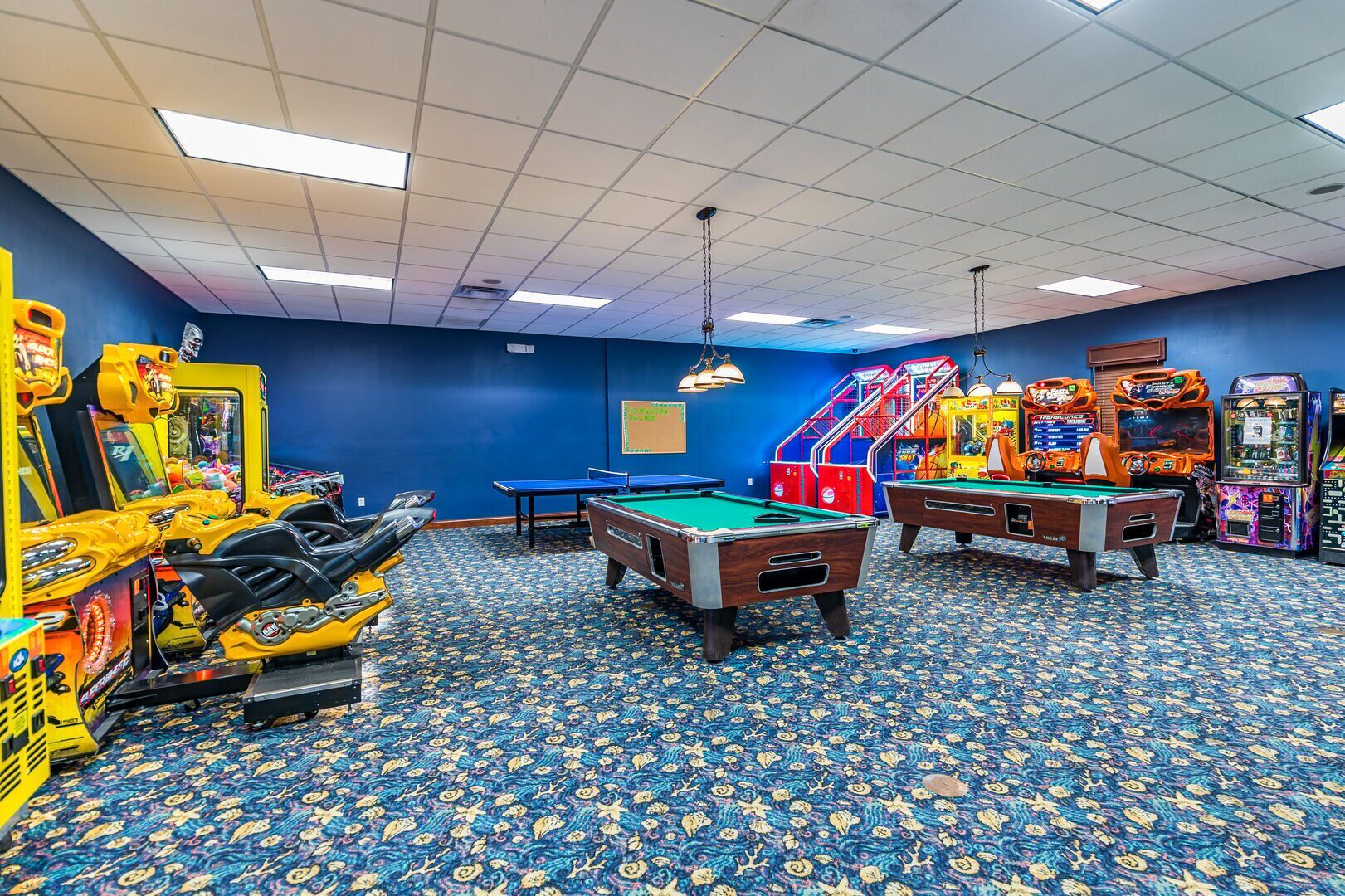 A room with pool tables, arcade games, and a blue carpet with a floral pattern.
