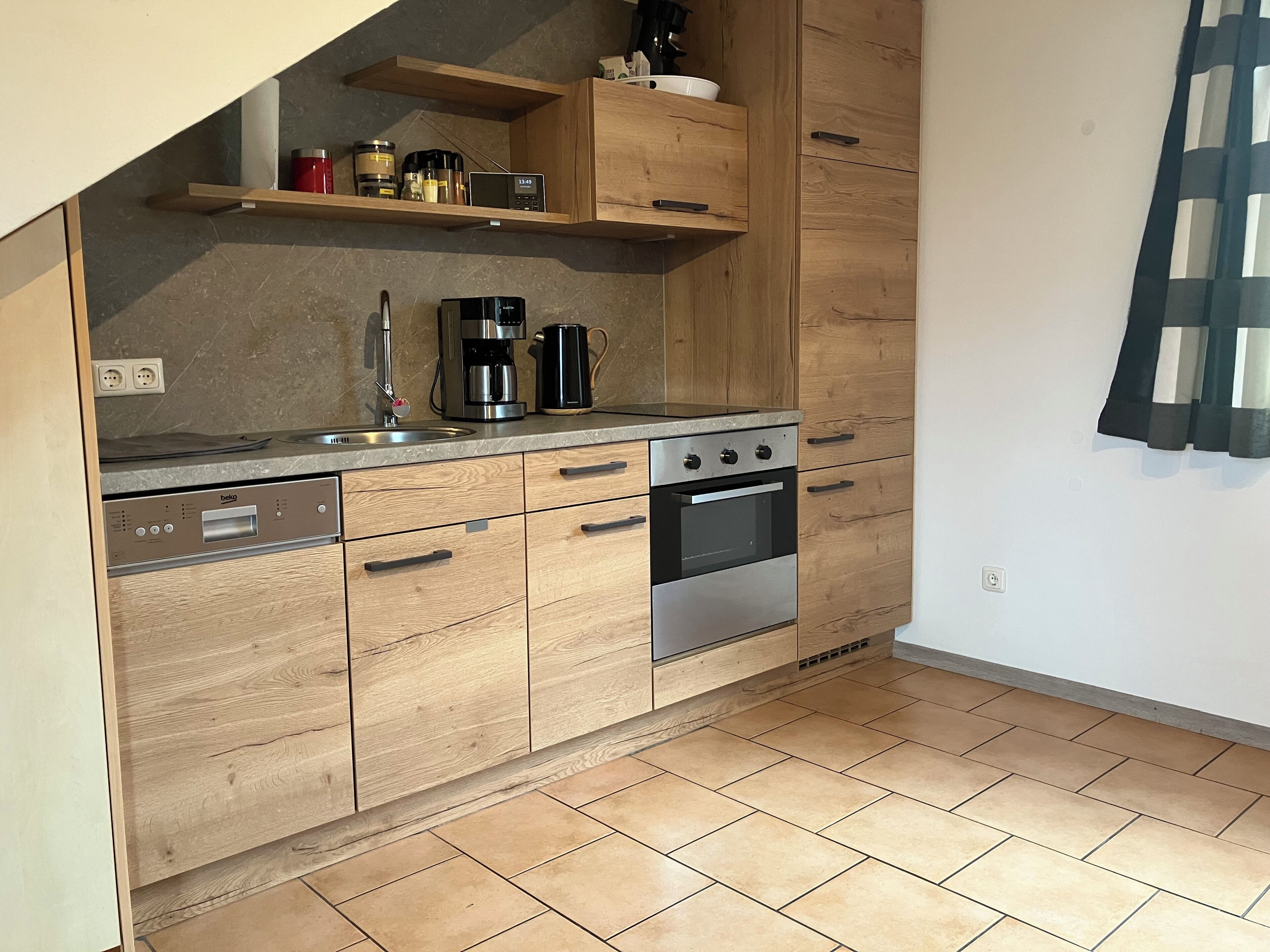 Une cuisine moderne avec des meubles en bois, un four encastré, une machine à café et un évier.