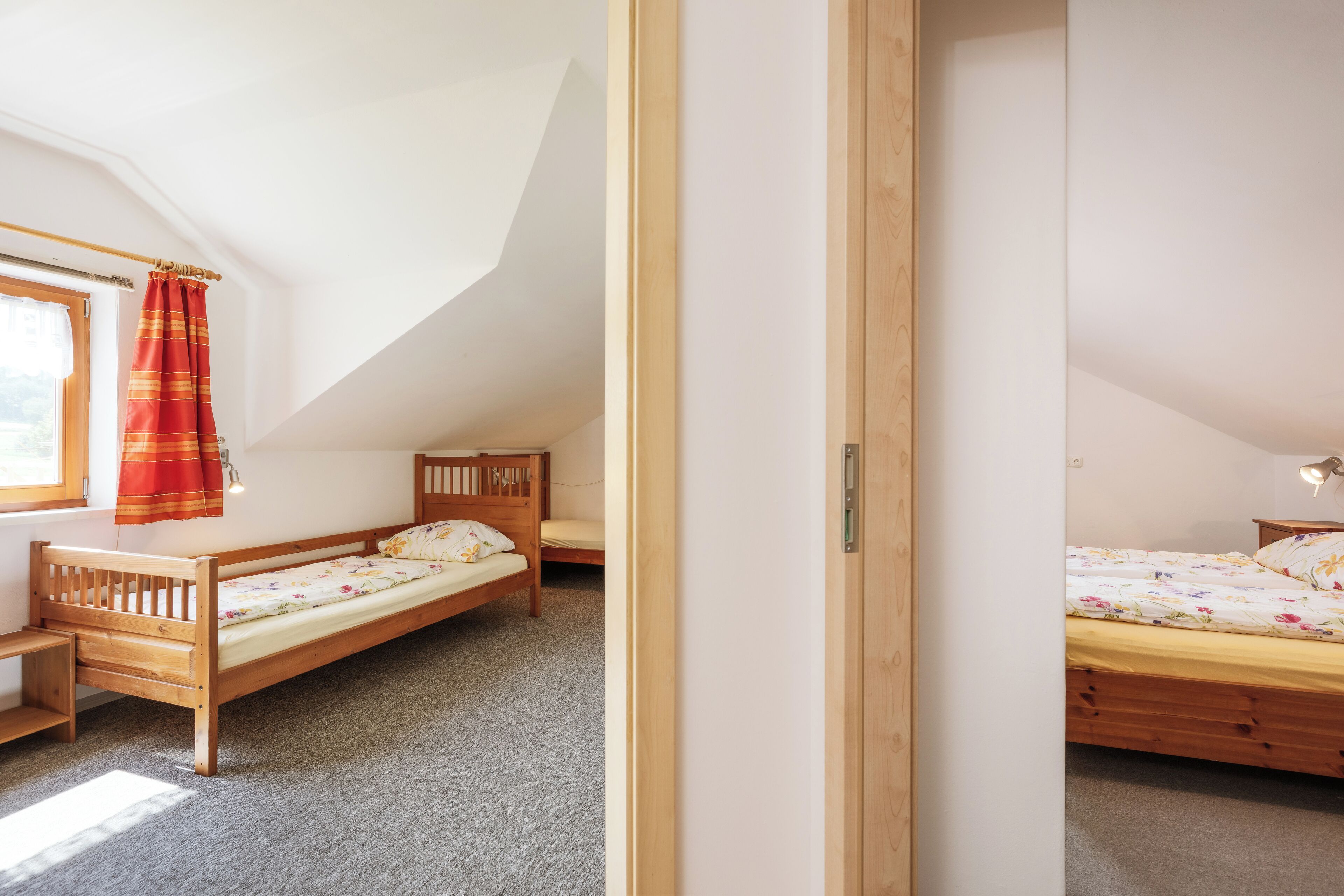 A bedroom with two wooden beds, a window with a curtain, and a door.