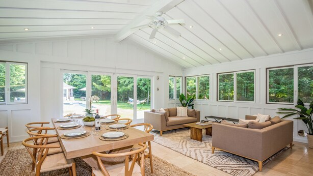 A spacious living area with a dining table set for four, a sofa, and a coffee table. - Cozy 6-bedroom beach house with pool, hot tub & AC in the Hamptons (Quogue)