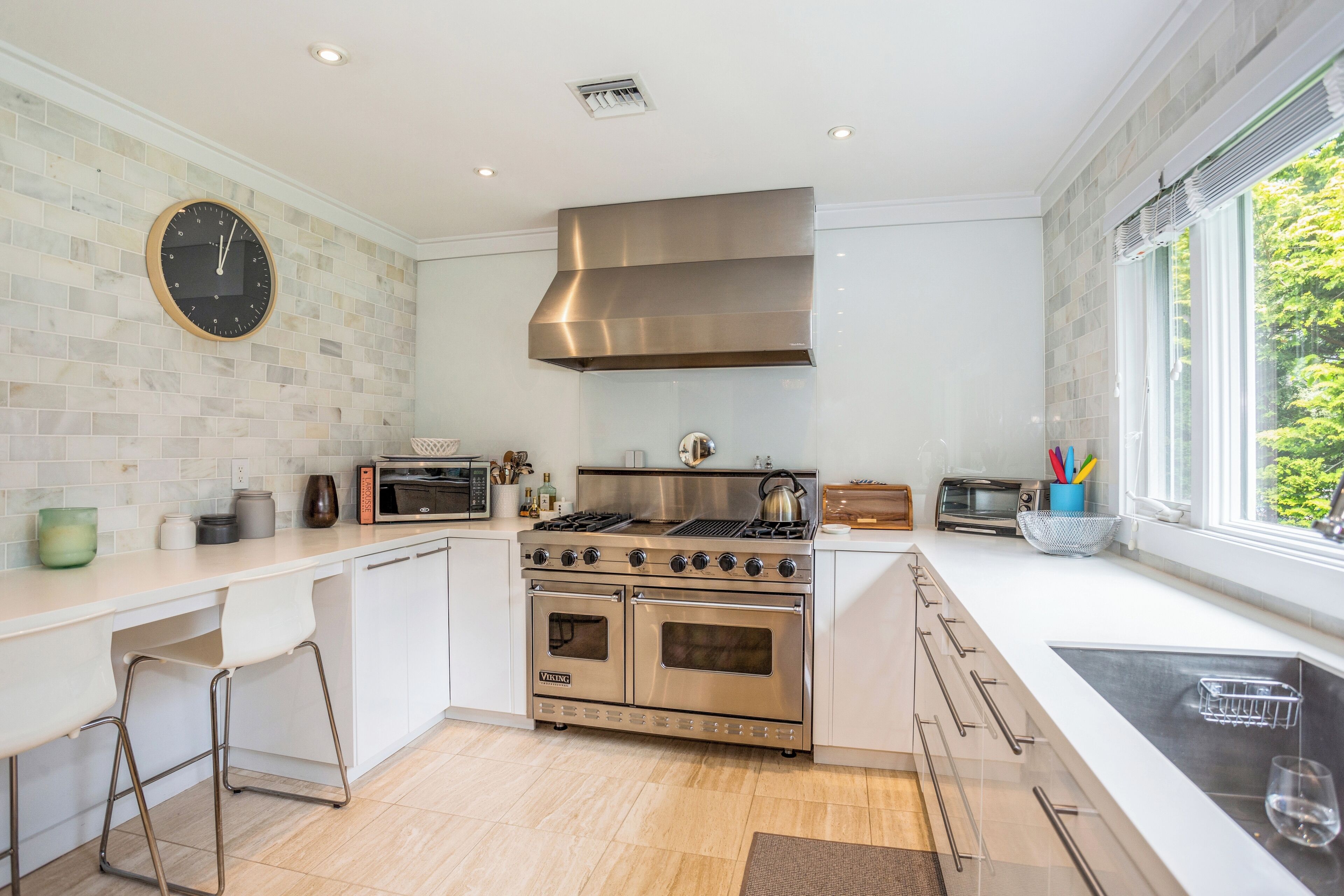 A modern kitchen with a stainless steel stove, white cabinetry, and a large window providing a view of greenery outside.