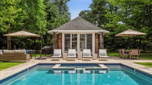 A swimming pool with lounge chairs and umbrellas, surrounded by trees. - Cozy 6-bedroom beach house with pool, hot tub & AC in the Hamptons (Quogue)