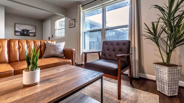 Una sala de estar con un sofá de cuero marrón, una mesa de centro de madera, un sillón tapizado y una planta en maceta.