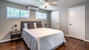 Un dormitorio con cama, mesitas de noche, aire acondicionado, ventilador de techo y dos puertas.