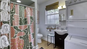 A bathroom with a shower curtain featuring a floral pattern, a toilet, a sink, and a stacked washer and dryer. - 1 Bedroom Spanish Bungalow Guest House (Holly Hill)