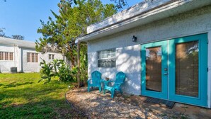 A single-story house with a white exterior and teal accents, featuring a front porch with two chairs and a small table. - 1 Bedroom Spanish Bungalow Guest House (Holly Hill)