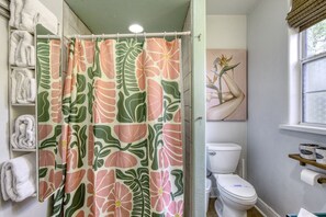 A bathroom with a shower curtain featuring a floral pattern, a toilet, and a shelf with rolled towels.