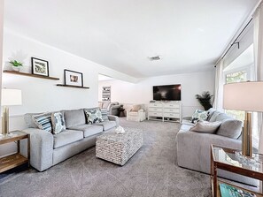 Una sala de estar moderna con dos sofás grises, una mesa de centro, un televisor y un mueble blanco.