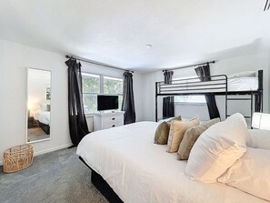Un dormitorio con una cama grande, televisión, cómoda y ventana con cortinas.
