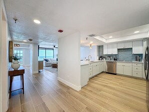 Una cucina moderna con mobili bianchi, un frigorifero in acciaio inossidabile e un pavimento in legno. Si nota anche un'area pranzo con un tavolo e delle sedie sullo sfondo.
