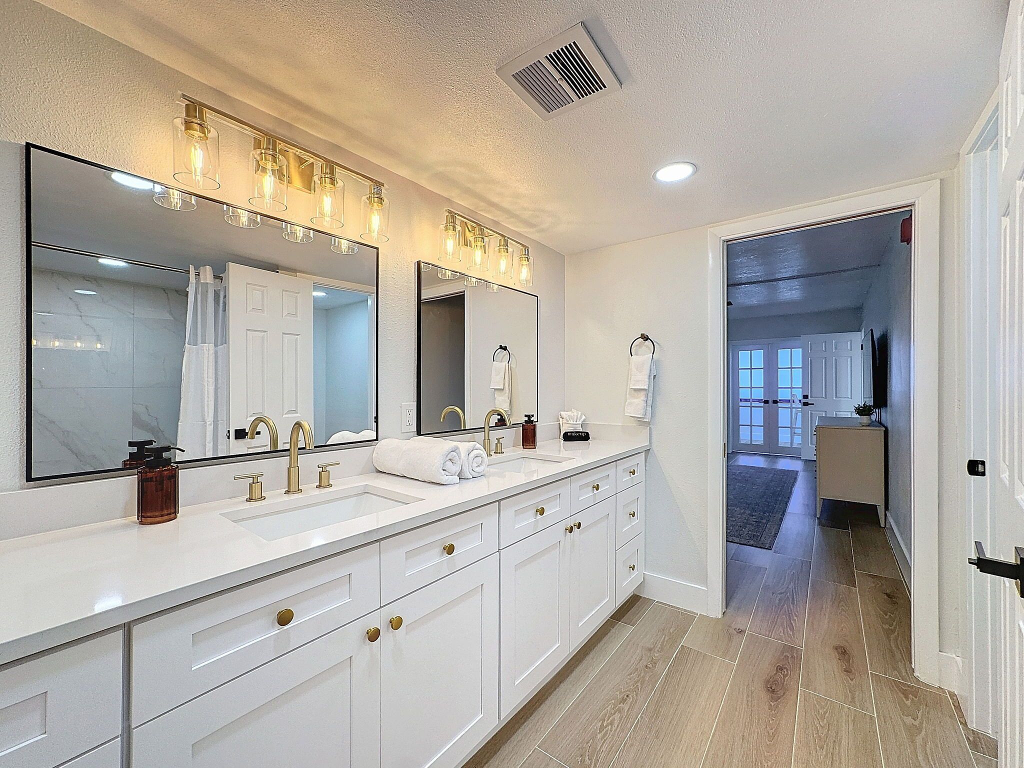 A modern bathroom with a large mirror, dual sinks, and a vanity with drawers.