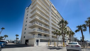 A multi-story hotel with balconies, a parking area, and palm trees. - 20002 Gulf Blvd, Penthouse 5 (Indian Shores)
