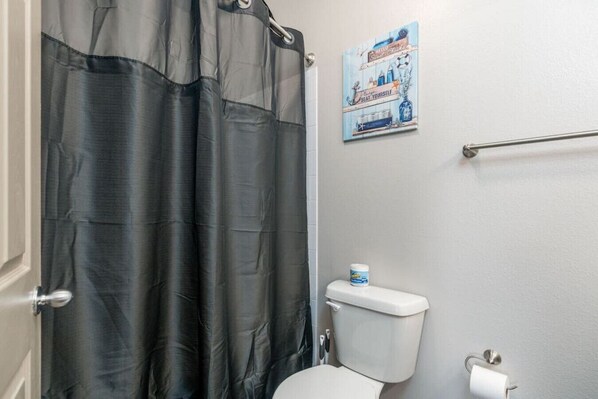 Une salle de bain avec un rideau de douche noir, des toilettes, une barre d’appui et une affiche accrochée au mur.